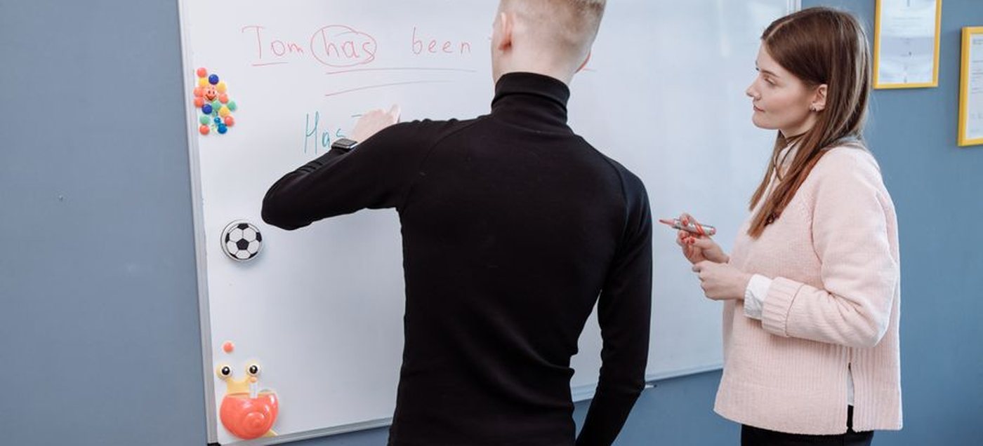 Profesora y alumno en una clase de inglés frente al pizarrón